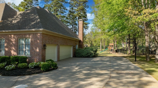 view of side of home with a chimney, a playground, concrete driveway, brick siding, and an attached garage