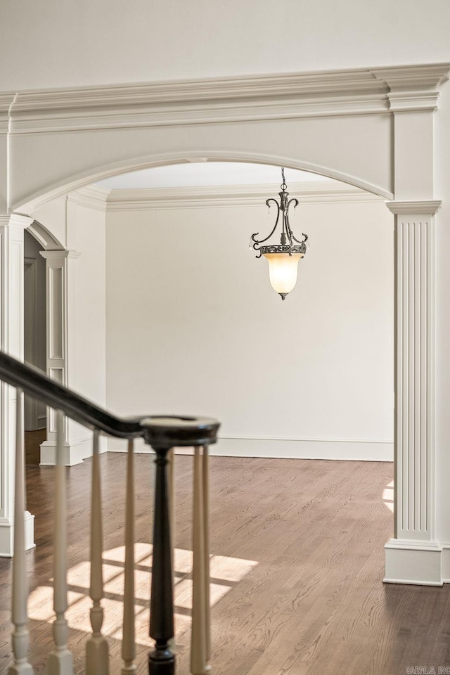 interior space featuring arched walkways, wood finished floors, crown molding, and decorative columns
