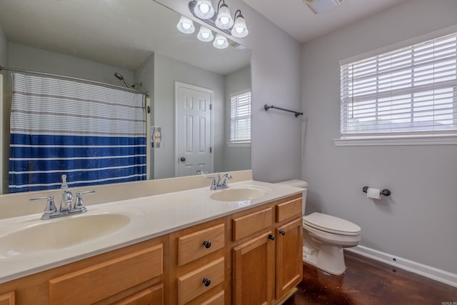 bathroom with baseboards, toilet, a sink, and double vanity
