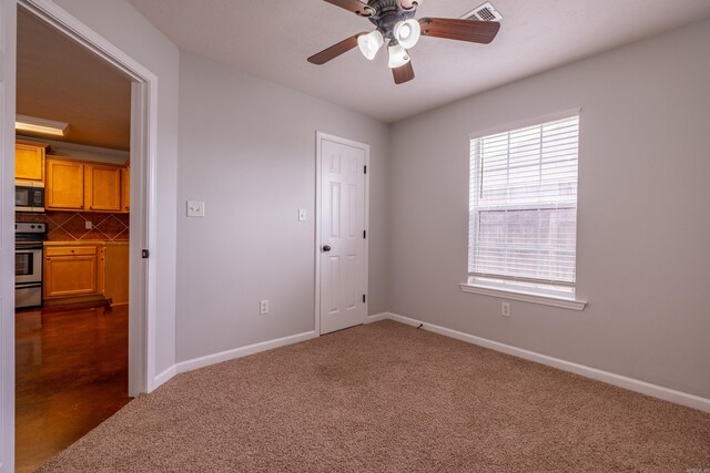 unfurnished room featuring baseboards, a ceiling fan, dark colored carpet, and visible vents