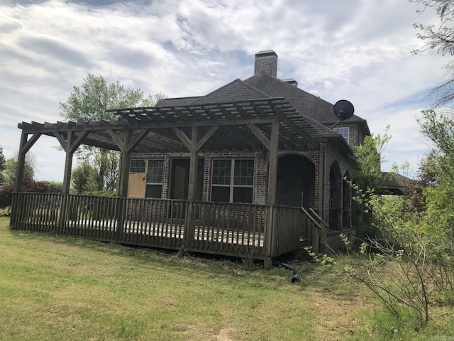 back of property with a pergola, a lawn, a chimney, a wooden deck, and brick siding