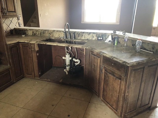 kitchen featuring light tile patterned flooring, dark brown cabinetry, light stone counters, and a sink
