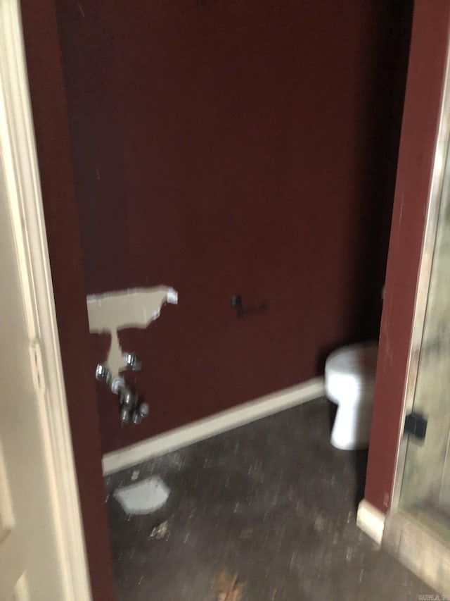 bathroom with a shower with shower door, toilet, and baseboards