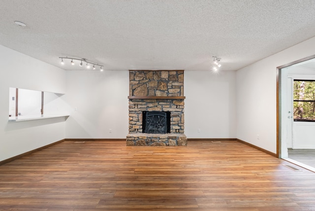 unfurnished living room featuring rail lighting, a stone fireplace, wood finished floors, and a textured ceiling