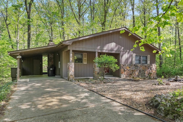view of front of house with concrete driveway, a chimney, an attached carport, and stone siding