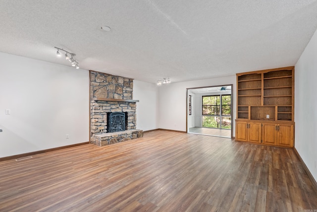 unfurnished living room with track lighting, wood finished floors, a textured ceiling, and a stone fireplace