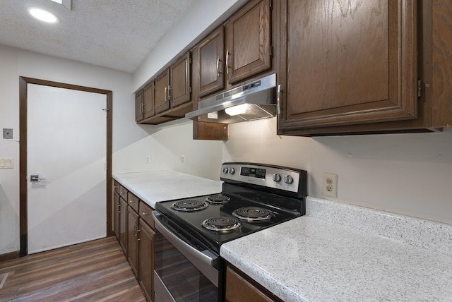 kitchen with dark wood-style floors, under cabinet range hood, light countertops, dark brown cabinets, and stainless steel electric range oven
