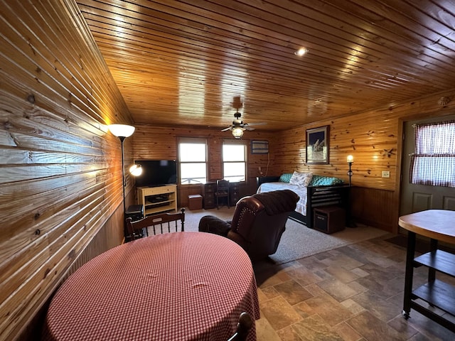 dining space with a ceiling fan, stone finish floor, wood walls, and wood ceiling