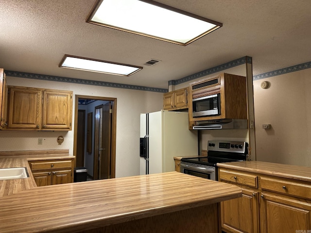 kitchen with a textured ceiling, wooden counters, stainless steel appliances, under cabinet range hood, and visible vents