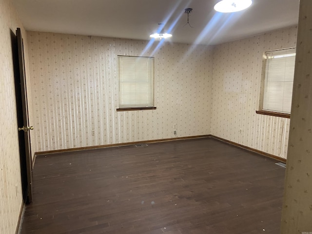 spare room with wallpapered walls, wood finished floors, visible vents, and baseboards