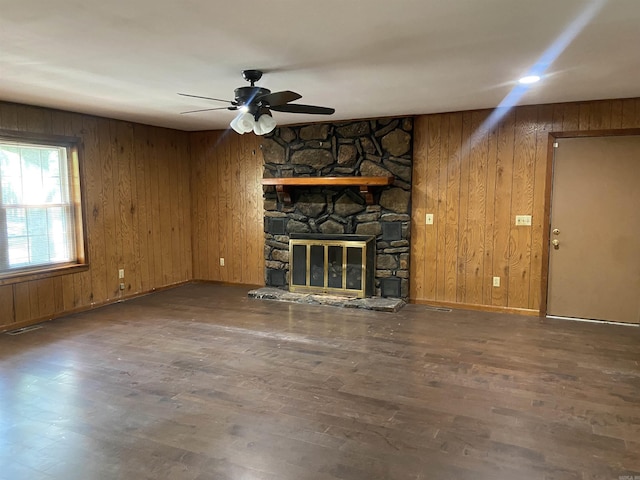 unfurnished living room with ceiling fan, wood finished floors, a stone fireplace, and wooden walls