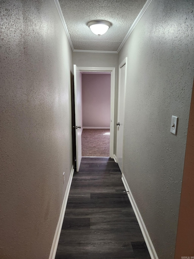 corridor with ornamental molding, wood finished floors, a textured wall, and a textured ceiling