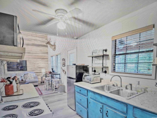 kitchen with a sink, freestanding refrigerator, ceiling fan, blue cabinetry, and stovetop