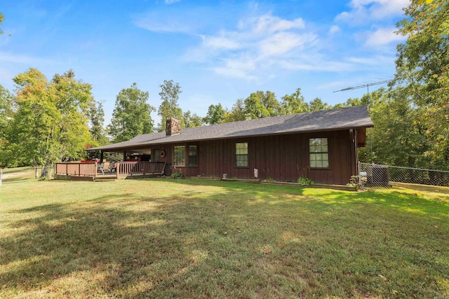 rear view of house featuring a chimney, a lawn, a deck, board and batten siding, and fence