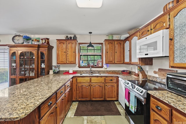 kitchen with brown cabinetry, a peninsula, a sink, and white appliances