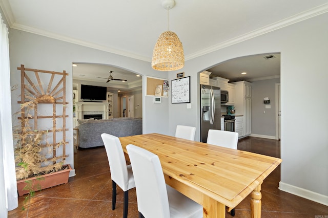 dining space featuring ornamental molding, arched walkways, baseboards, a fireplace, and ceiling fan