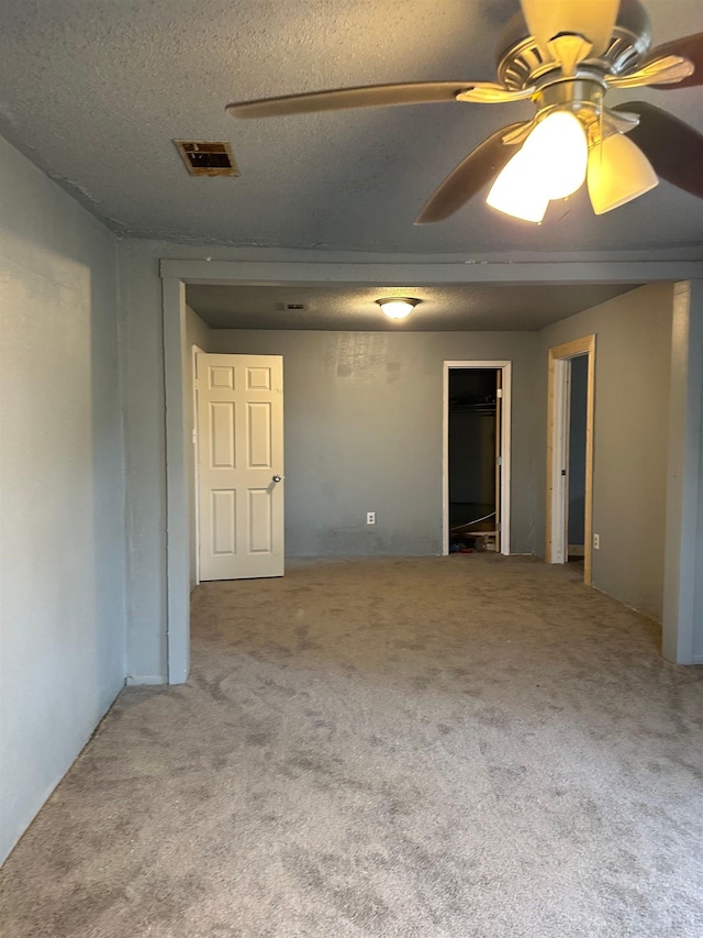 unfurnished room with a textured ceiling, visible vents, carpet flooring, and a ceiling fan