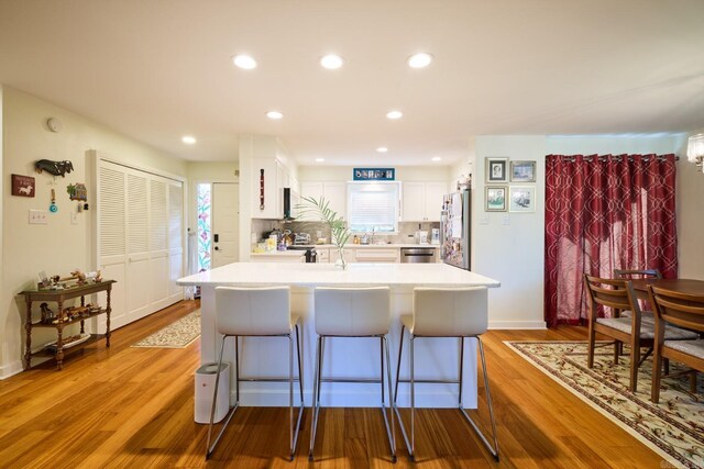 kitchen featuring white cabinets, a kitchen breakfast bar, light countertops, light wood-style flooring, and appliances with stainless steel finishes