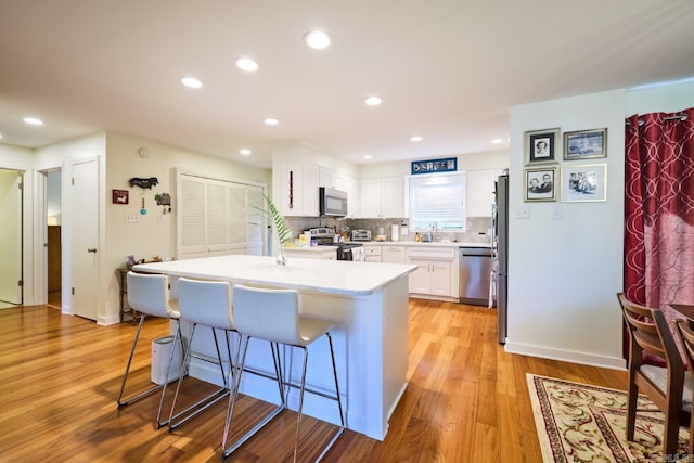 kitchen with a kitchen breakfast bar, light wood-type flooring, stainless steel appliances, light countertops, and white cabinetry