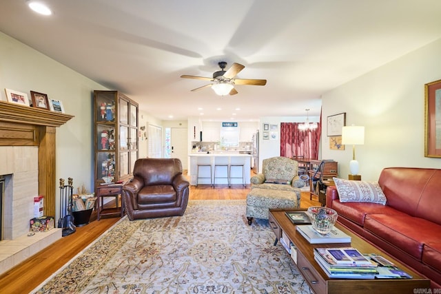 living area featuring ceiling fan with notable chandelier, a tile fireplace, recessed lighting, and light wood-style floors