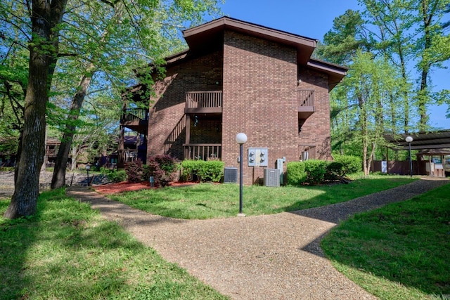 view of home's exterior with brick siding, a yard, central air condition unit, and a balcony