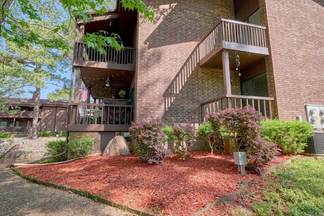 view of side of home featuring ceiling fan, a balcony, and brick siding