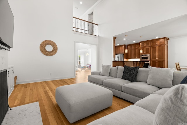 living area with baseboards, recessed lighting, a towering ceiling, and light wood-type flooring