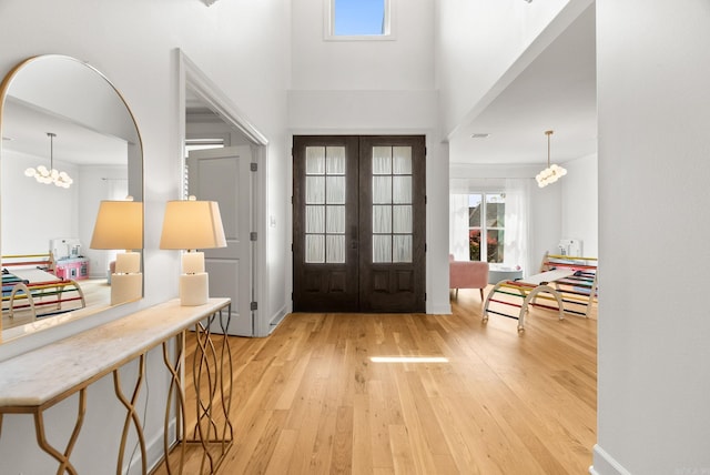 entrance foyer featuring an inviting chandelier, light wood-style flooring, a high ceiling, and french doors