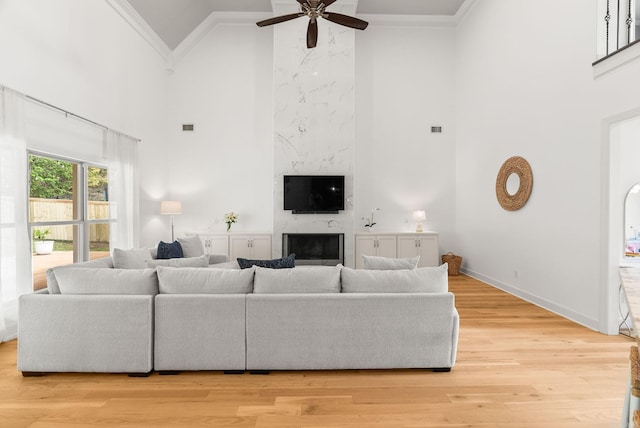 living room with baseboards, a premium fireplace, a ceiling fan, crown molding, and high vaulted ceiling
