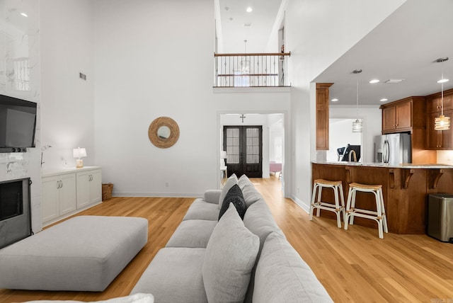 living room featuring light wood-style floors, french doors, baseboards, a high ceiling, and recessed lighting