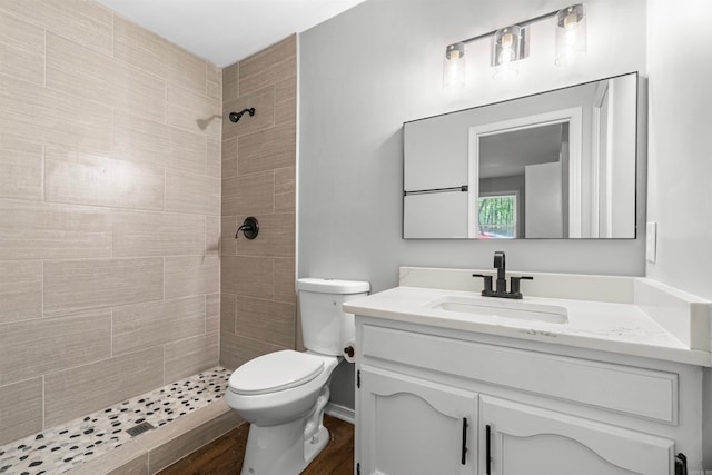 bathroom with toilet, wood finished floors, vanity, and a tile shower
