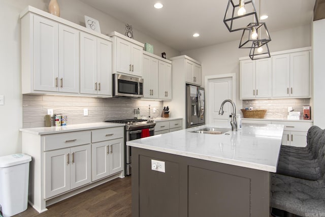 kitchen featuring stainless steel appliances, a kitchen island with sink, a sink, and backsplash