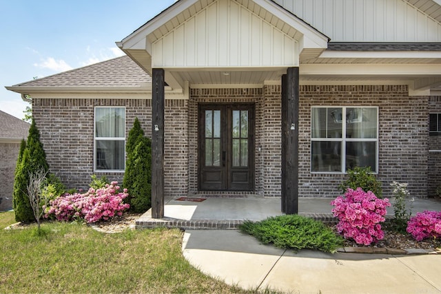 view of exterior entry with brick siding, roof with shingles, and a porch