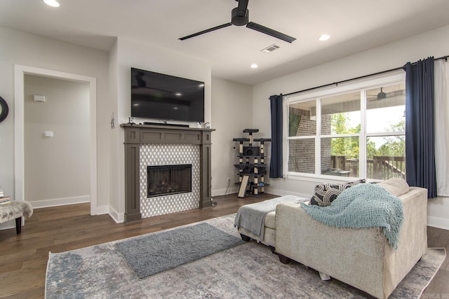 living room with a ceiling fan, wood finished floors, visible vents, and a tiled fireplace
