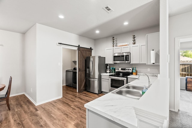 kitchen with a barn door, a sink, washer and dryer, stainless steel appliances, and visible vents