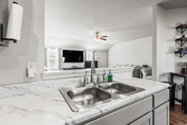 kitchen with a textured ceiling, open floor plan, ceiling fan, and a sink