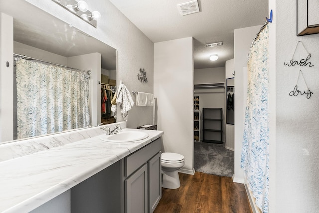 bathroom with toilet, vanity, wood finished floors, and visible vents