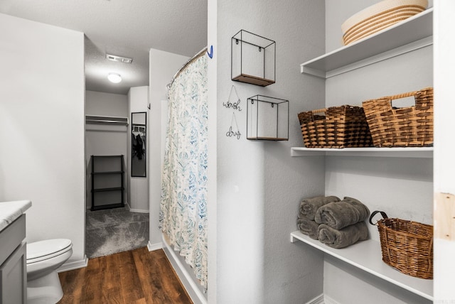 bathroom with toilet, visible vents, wood finished floors, vanity, and a walk in closet