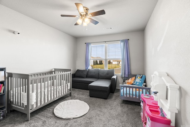 carpeted bedroom with a crib, a ceiling fan, and visible vents