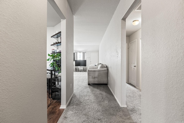 corridor featuring a textured wall, visible vents, baseboards, and carpet