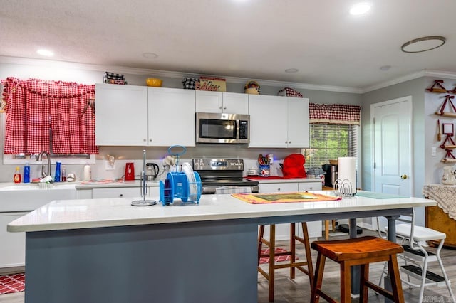 kitchen with light countertops, white cabinetry, appliances with stainless steel finishes, and ornamental molding