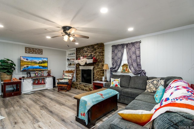 living area with recessed lighting, wood finished floors, ceiling fan, crown molding, and a stone fireplace