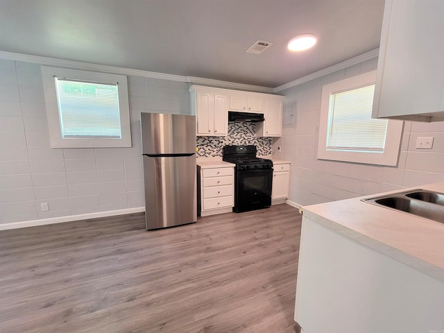 kitchen with ornamental molding, black gas range oven, under cabinet range hood, visible vents, and freestanding refrigerator
