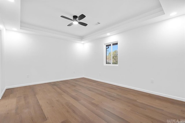 unfurnished room with wood finished floors, a tray ceiling, baseboards, visible vents, and recessed lighting