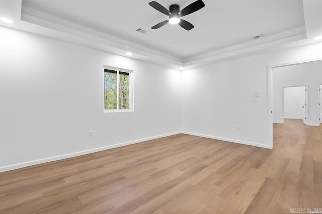 spare room with a ceiling fan, a tray ceiling, visible vents, and light wood-type flooring