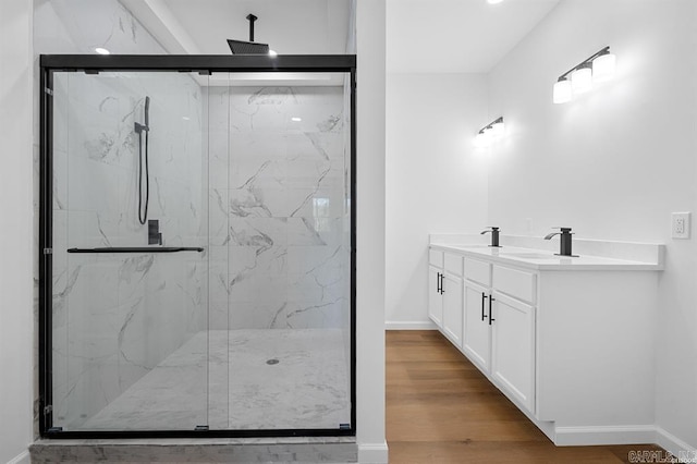 bathroom featuring baseboards, wood finished floors, a marble finish shower, and a sink