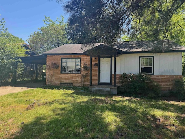 view of front of property with an attached carport, brick siding, a shingled roof, board and batten siding, and a front yard