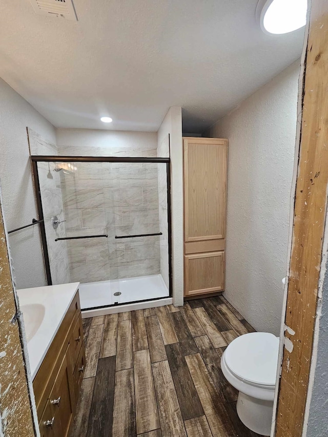 full bathroom with toilet, wood finished floors, a shower stall, a textured wall, and vanity