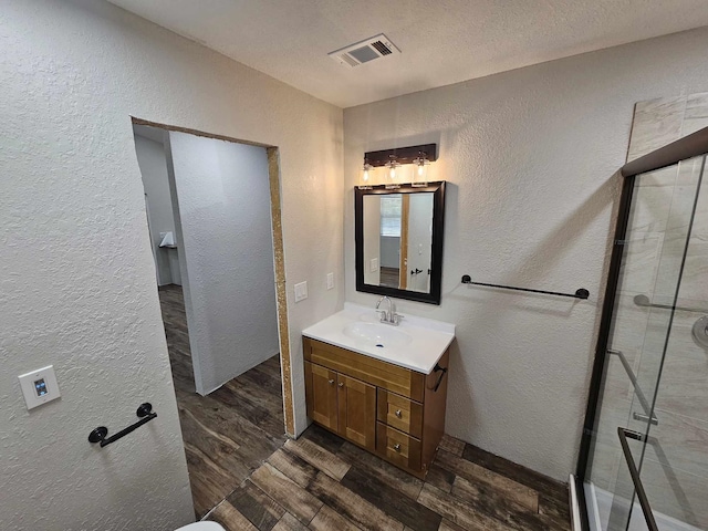 bathroom with a textured ceiling, visible vents, wood finished floors, a textured wall, and vanity