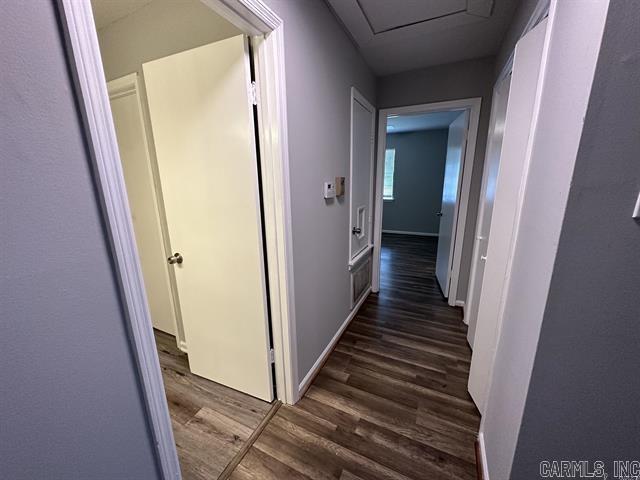 hallway featuring attic access, baseboards, and dark wood-style flooring